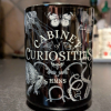 Black Mug with White Letters Saying Cabinet of Curiosities and White Sketches of Animals like butterflies and jellyfish and tentacles